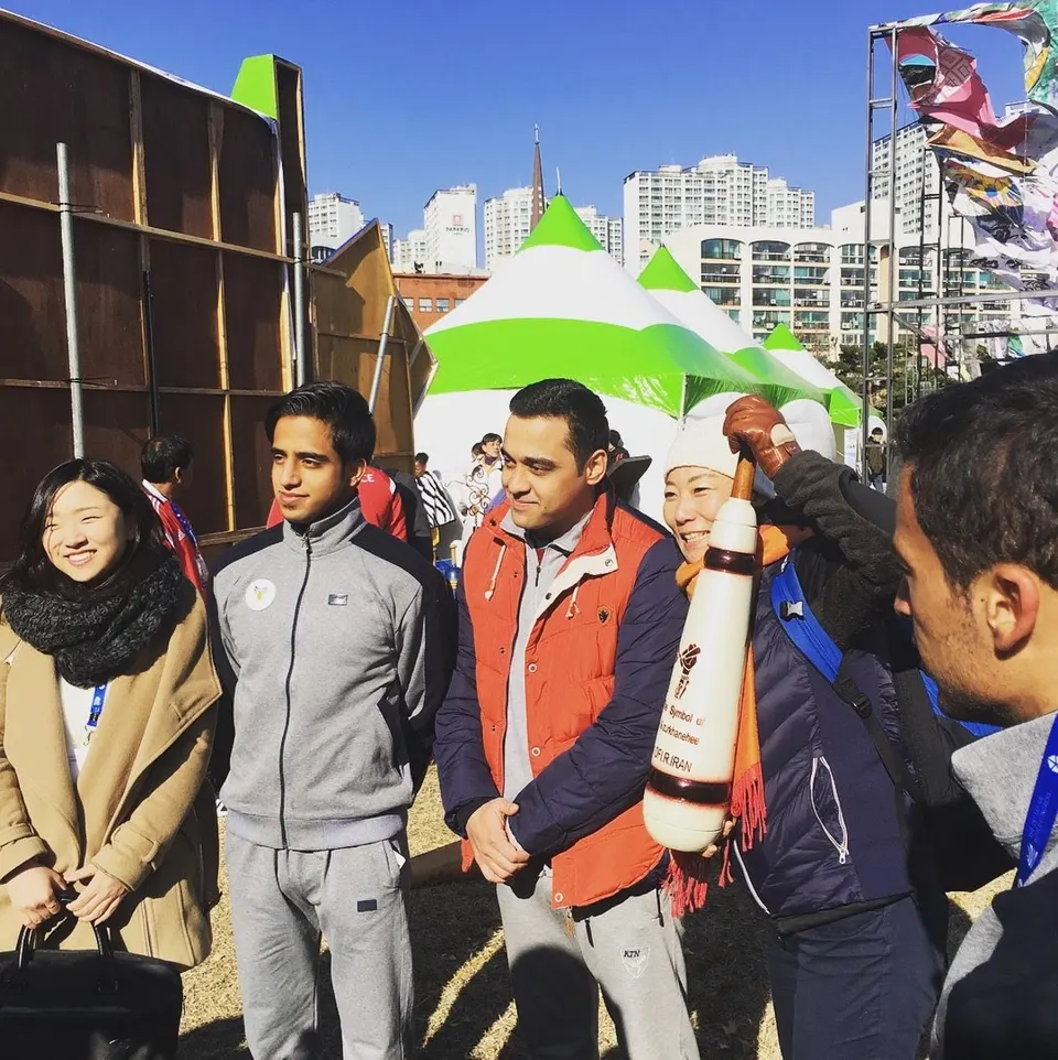 초록 · 흰 천막 앞에 선 사람들 가운데 털모자를 쓴 사람이 흰 페르시안밀을 들고 웃는다