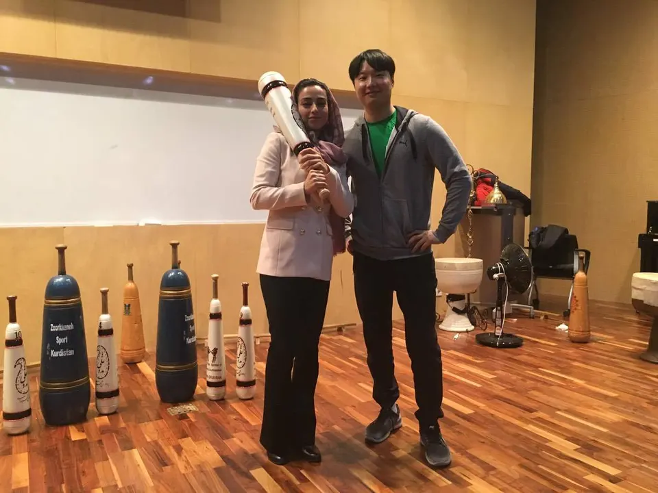 히잡을 쓴 사람이 흰 페르시안밀을 어깨에 멨고 곁에 회색 후드 차림의 사람이 섰다, 바닥엔 페르시안밀들