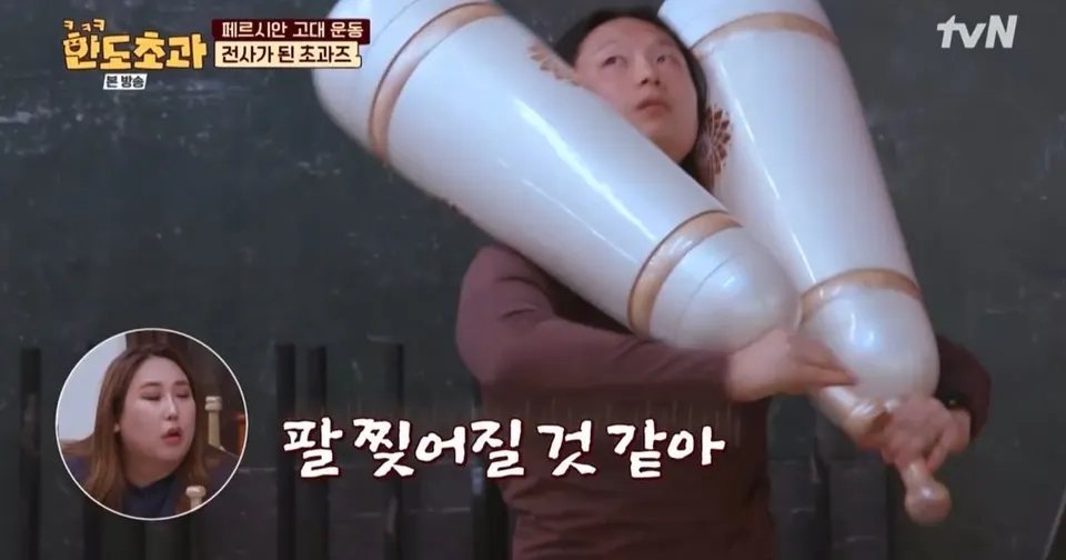 흰 페르시안밀 두 개를 어깨에 멘 사람이 버티고, 자막은 「팔 찢어질 것 같아」, 아래 원 안에 다른 출연자