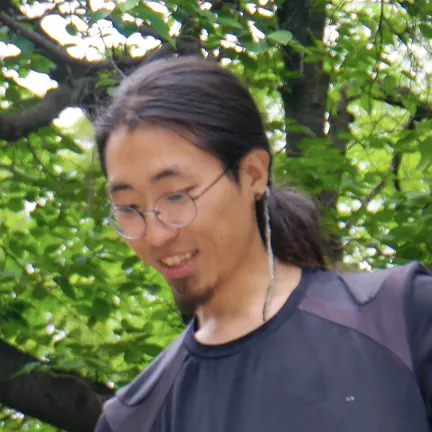 초록 나뭇잎을 배경으로 웃고 있는 안경 쓴 긴 머리 사람의 얼굴