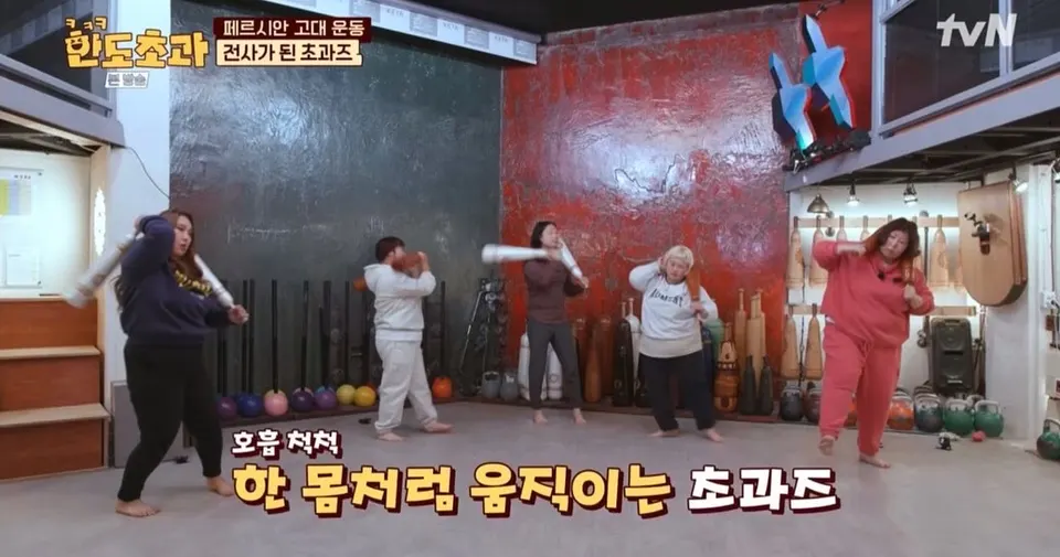운동실에서 다섯 명이 흰 방망이를 함께 휘두르고, 자막은 「호흡 척척 한 몸처럼 움직이는 초과즈」