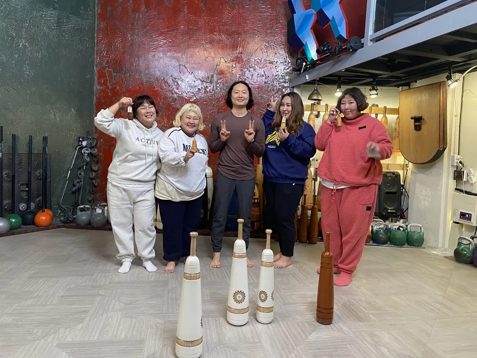 다섯 명이 브이를 하거나 작은 방망이를 들고 서 있고, 앞 바닥에 페르시안밀 넷이 세워져 있다