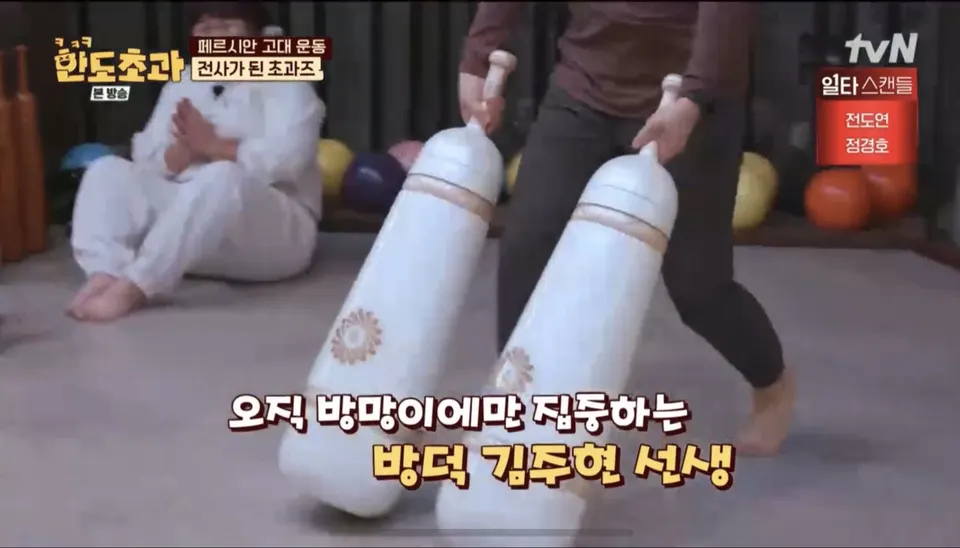 큰 흰 페르시안밀 두 개를 세워 쥐고 옮기는 사람, 자막은 「오직 방망이에만 집중하는 방덕 김주현 선생」