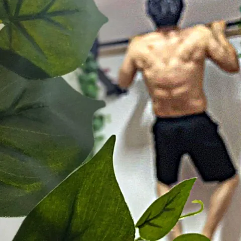 잎 너머, 웃통을 벗고 철봉을 잡은 방덕의 뒷모습